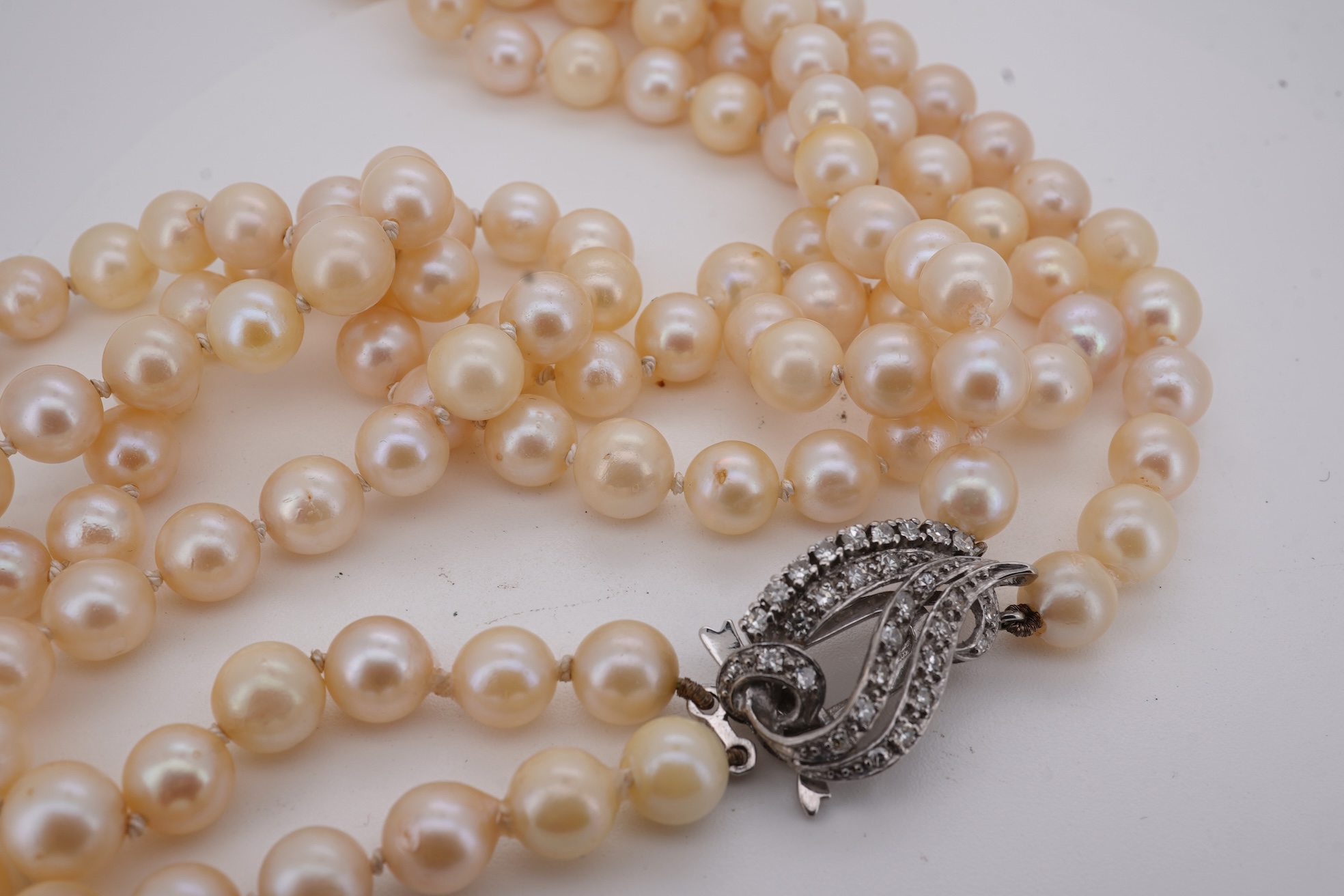A twin strand cultured pearl necklace with a diamond cluster set white metal scroll shaped clasp, 60cm.